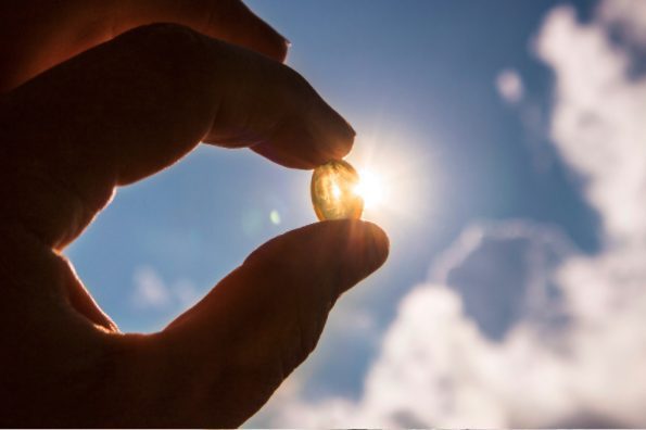 Holding a vitamin D capsule with the sky in the background