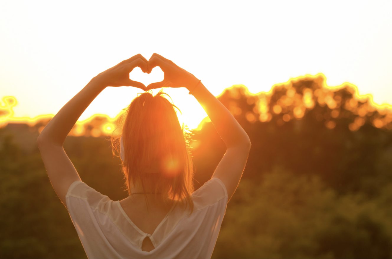 Woman showing a heart sign with her hand during sunset
