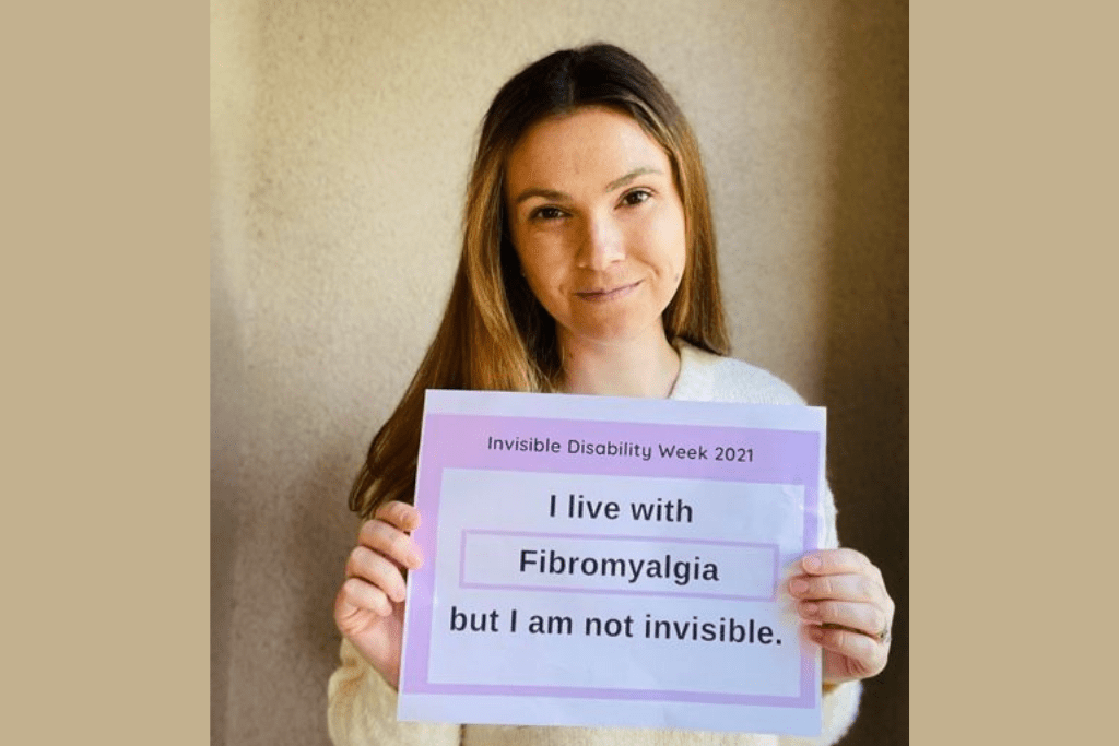 Young woman holding a card that says 'I live with fibromyalgia but I am not invisible'